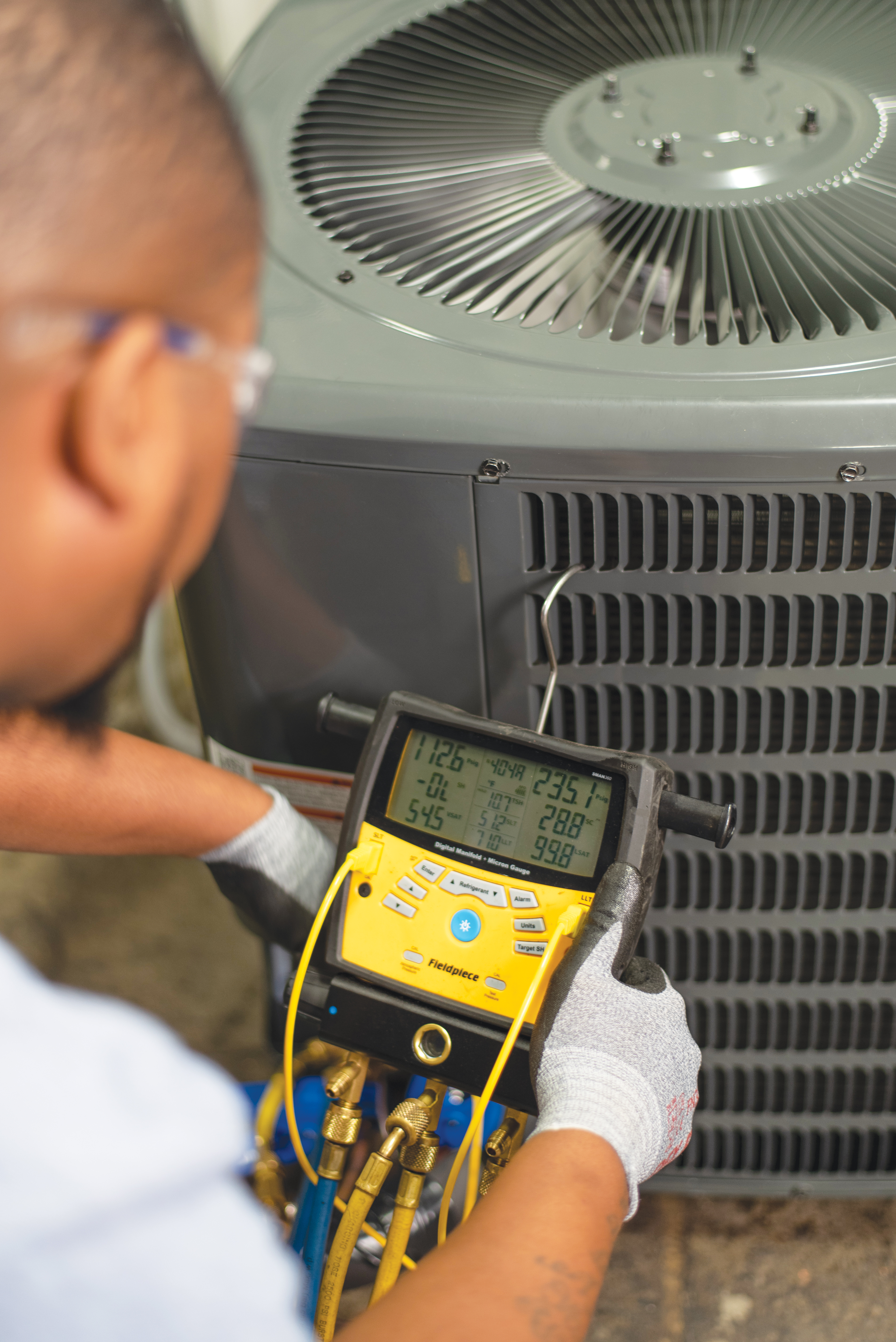 Male holding a refrigerant manifold by an air conditioner
