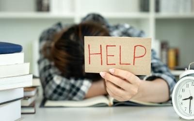 Person with their head down on a desk holding a sign that says help